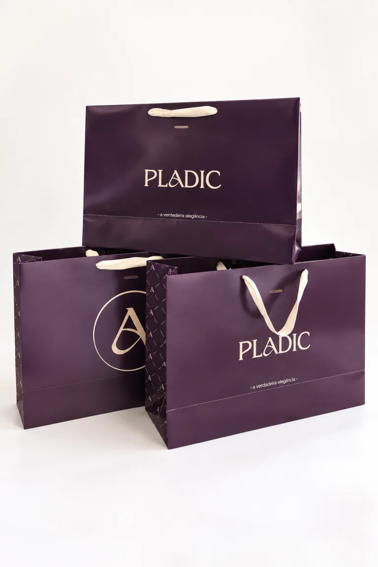 Conjunto de sacolas premium Pladic em papel roxo com impressão clara e alças de fita.
