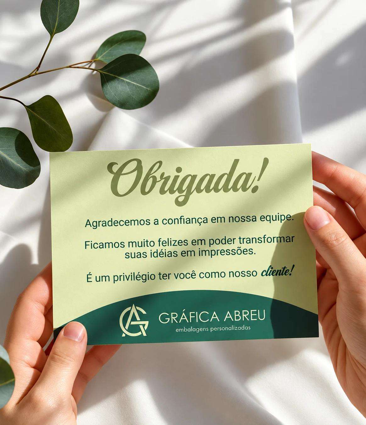 Cartão de agradecimento da Gráfica Abreu segurado pelas mãos de uma pessoa.